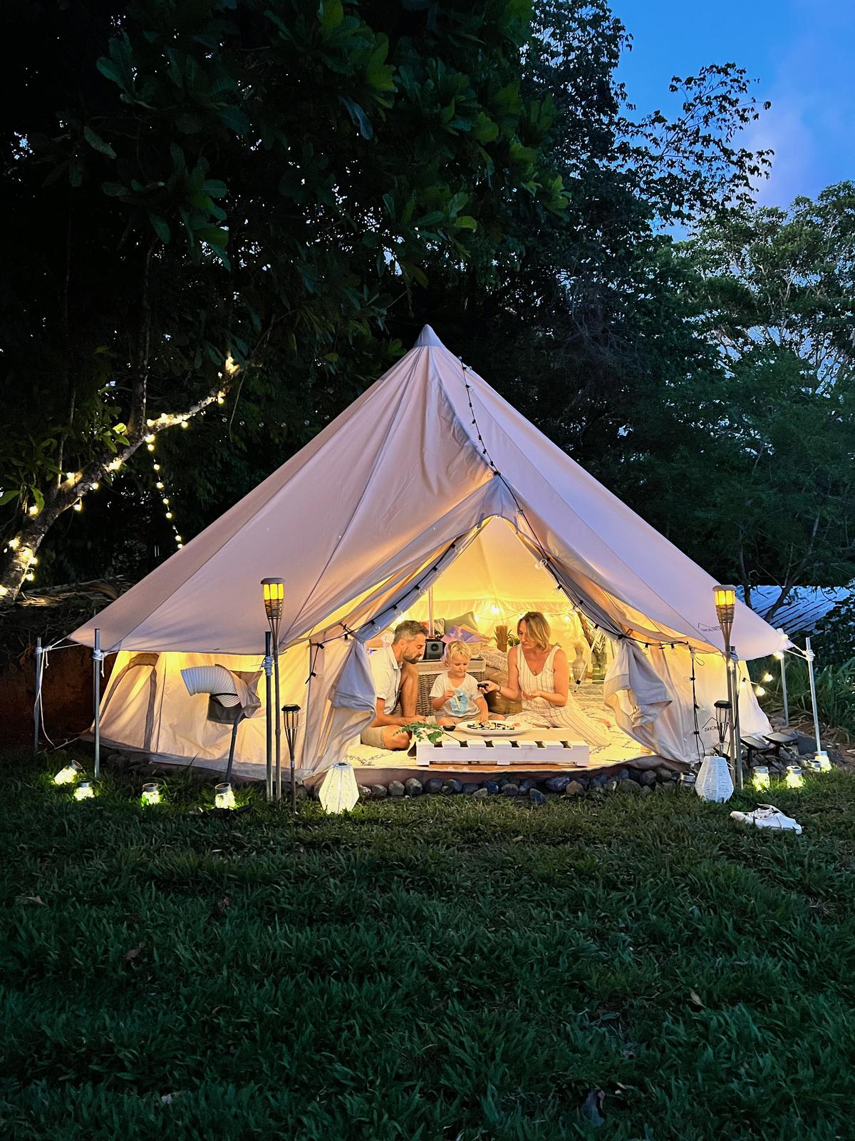 An evening at Columbus Heights — glamping tent at dusk, warm lamplight, fairy lights in the trees